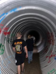 two people are walking through a pipe with graffiti on it