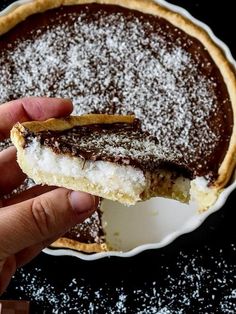 a hand holding a piece of pie with powdered sugar on top, in front of a pie pan