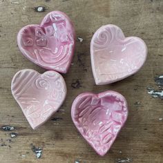 three pink heart shaped dishes sitting on top of a wooden table