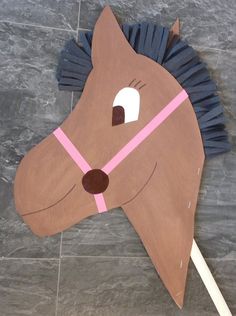 a cardboard horse head with a pink ribbon around it's neck on a tile floor