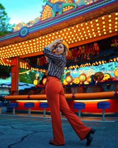 a woman is dancing in front of a carnival ride at night with her hands behind her head