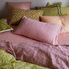 a bed with pink and green pillows on top of it next to a white headboard