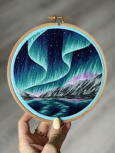 someone is holding up their embroidery project with an image of the northern lights on it