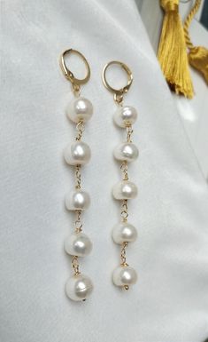 These elegant pearl earrings are perfect for creating a refined and sophisticated look. They add a touch of luxury and elegance to any outfit. Materials: Pearls, golden metal Design: Classic string of pearls connected with golden metal elements. Dimensions: Earring length - 8.5 cm Closure: Comfortable and secure ring clasp. Design Description: Each earring consists of five large white pearls, securely fastened together. The pearls are evenly spaced, creating the effect of a graceful long string. Long Pearl Earrings, String Of Pearls, Golden Ring, Metal Design, Large White, Long Earrings, Pearl White, Favorite Jewelry, Timeless Design