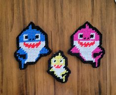 three pieces of bead art depicting cartoon characters on a wooden table with scissors and thread