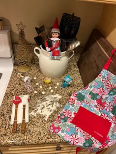 an elf is sitting on top of the kitchen counter next to his cooking utensils