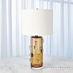 a table lamp sitting on top of a white counter next to a curtained window