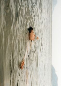 a woman in white shirt standing next to a wall with water coming out of it