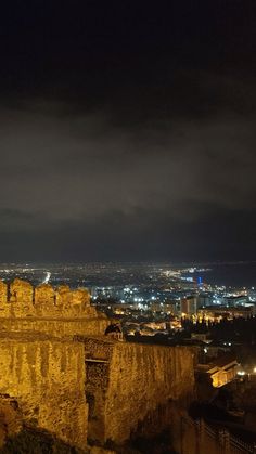 the city lights shine brightly in the dark night sky over an old castle like structure