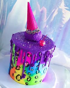 there is a colorful cake with a pink hat on top and purple icing around it