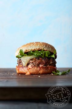 a hamburger with lettuce and other toppings sitting on top of a wooden table