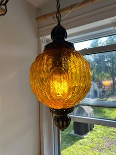 a yellow glass light hanging from a ceiling in front of a window with grass outside