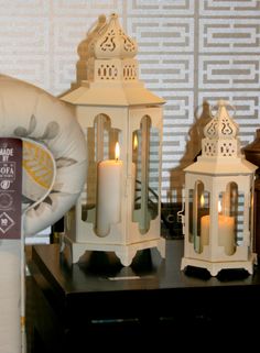 three white lanterns sitting on top of a table next to a pillow and candle holder