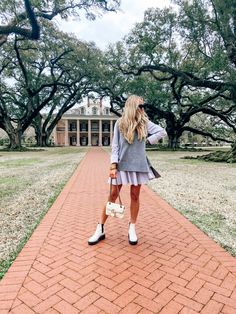 a woman walking down a brick path with trees in the background