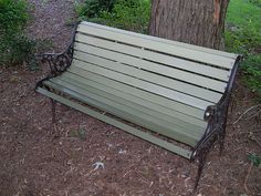 a park bench sitting next to a tree in the grass near a path and trees