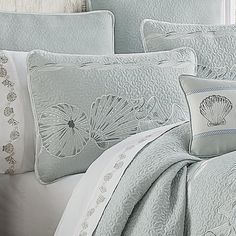 the comforter is made up with white and blue pillows, along with seashells