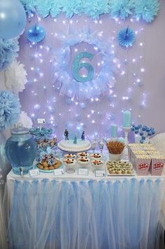 a table topped with lots of desserts and blue decorations on top of a white table cloth