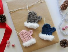 crocheted mittens and gloves are tied to a brown paper with red ribbon