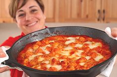 a woman holding up a large skillet filled with meat and cheese on top of it