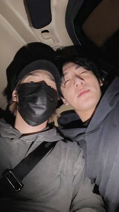 two people in the back seat of a car wearing black masks and covering their faces