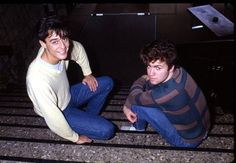 two young men sitting on the ground next to each other