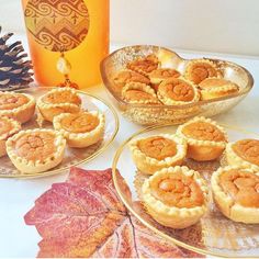 several small desserts are on plates next to a pine cone and glass jar with an orange liquid