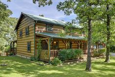 a log cabin sits in the middle of a grassy area surrounded by trees and shrubs