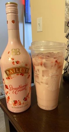 a bottle of bailey's strawberry cream next to a plastic cup filled with liquid