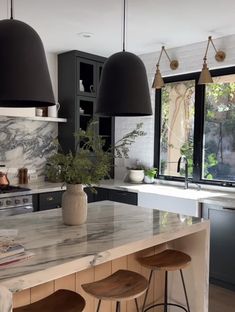 a kitchen with marble counter tops and black pendant lights hanging from the ceiling over the island