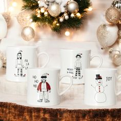 three coffee mugs with cartoon characters on them sitting in front of a christmas tree