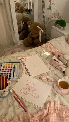 a teddy bear sitting on top of a bed next to a table with markers and pencils