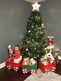 a small child sitting on two boxes in front of a christmas tree with gifts under it