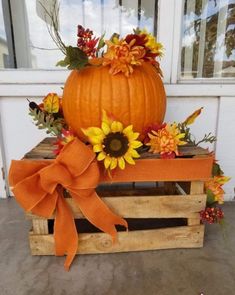 a pumpkin sitting on top of a wooden crate filled with flowers and sunflowers