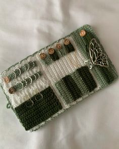 a green and white crochet purse with buttons, pins and earrings on it