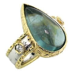 This cabochon tourmaline playfully exhibits pleochroism, showing two distinct colors from different viewing angles. Straight on, this gem shows a striking silvery blue shade. When viewed at an angle, a distinctly green blue tone emerges. "Sienna" features a bold, wearable style finished with layers of sumptuous detail. Every Sienna ring showcases a gemstone which was carefully chosen for maximum eye appeal, and the ring is then custom crafted around the gemstone. Sienna is a perfect option anytime. -8.86ct Indicolite Blue Tourmaline (Brazil) -0.10ct Diamonds -18kt Gold -made in Italy by Cynthia Scott Jewelry ABOUT THE TECHNIQUE This piece of jewelry was hand-fabricated and hand-engraved by goldsmiths in Florence, Italy. Florentine Engraving is an Old World jewelry making technique and styl Hand Engraved Rings, Sapphire Cocktail Ring, Indicolite Tourmaline, Gold Diamond Band, Engraved Ring, Blue Tourmaline, Gold Engraving, Diamond Cocktail Rings, Cabochon Ring