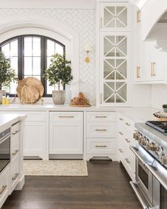 a kitchen with white cabinets and an oven in the center is decorated with potted plants