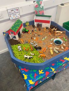 there is a toy farm in the sandbox with animals and other toys around it