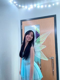 a girl in a blue dress with a green fairy wings on her back standing in front of a door