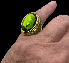 Wow! What a statement ring. This vintage ring has a large green either rhinestone or glass stone in the center surrounded by dainty white simulated diamonds on a 316L stainless steel which is the highest quality for jewelry. The band is then clothed in a gold tone overlay. The sides are decorated in green flames giving this ring more character, this is a very interesting piece of vintage costume jewelry. The size is 7.75 Green Oval Enamel Ring For Anniversary, Green Oval Enamel Anniversary Ring, Oval Green Enamel Anniversary Ring, Green Oval Enamel Ring For Formal Occasions, Oval Green Enamel Ring Gift, Elegant Green Crystal Ring With Metal Band, Formal Green Oval Enamel Ring, Formal Oval Green Enamel Ring, Elegant Green Crystal Ring