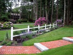 a white picket fence in the middle of a lush green yard with flowers and trees