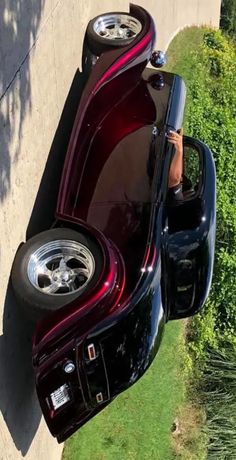 the back end of a classic car parked in front of a wall with grass and bushes