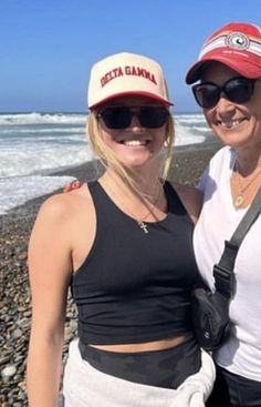 two women standing next to each other on a beach with the ocean in the background