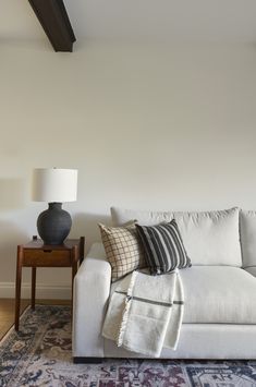 a living room with a white couch and pillows on the floor next to a lamp