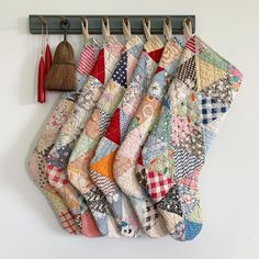 several pieces of colorful quilt hanging from hooks on a white wall next to brooms