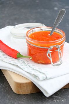 a glass jar filled with red sauce next to a pepper on top of a cutting board