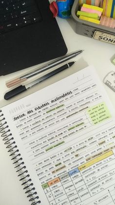 an open notebook sitting on top of a desk next to a pen and laptop computer