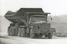 an old dump truck driving down a dirt road