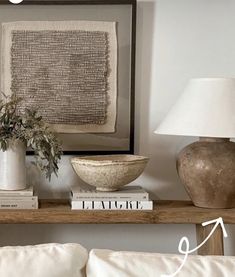 a table with books and vases on it next to a wall mounted art piece