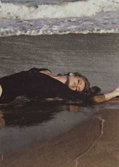 a woman is laying on the beach with her legs spread out and feet in the water