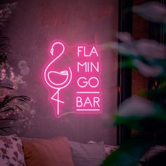 a pink neon sign that says flaming go bar in front of a couch and potted plant